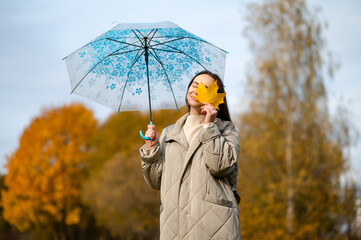 Autumn joy concept  - woman hiding one eye with maple leaf under umbrella