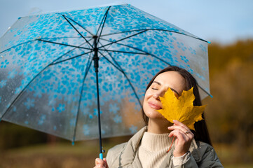 Autumn joy concept  - woman hiding one eye with maple leaf under umbrella