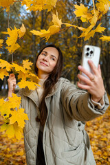 Autumn selfie concept – young woman smiling among yellow maple leaves