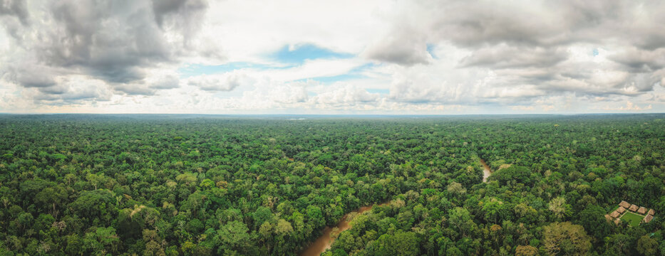 Aerial panoramic view of a vibrant tapestry of emerald rainforest interwoven with a winding river and small building, Tipishca, Sucumbios, Ecuador.