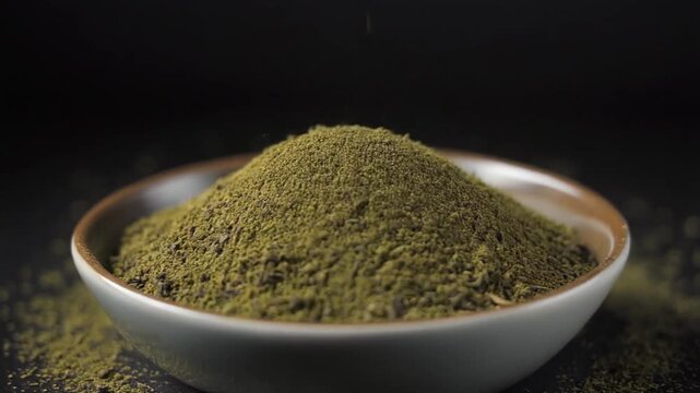 Green powder pouring into a ceramic bowl against a dark background.