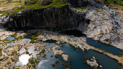 Aerial view of water bodies nestled among the rocky terrain, contrasting with the green vegetation atop the cliffs, Jos, Plateau, Nigeria.