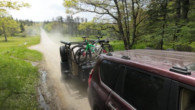 Traveling along a dusty forest road, a teardrop camper trailer tows bicycles for an adventure in Dolly Sods in slow motion, surrounded by lush greenery and Appalachian mountains.