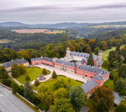 Aerial view of the majestic Sychrov Castle with its red facade and gray roofs surrounded by vibrant autumn foliage, Sychrov, Liberecky kraj, Czechia.
