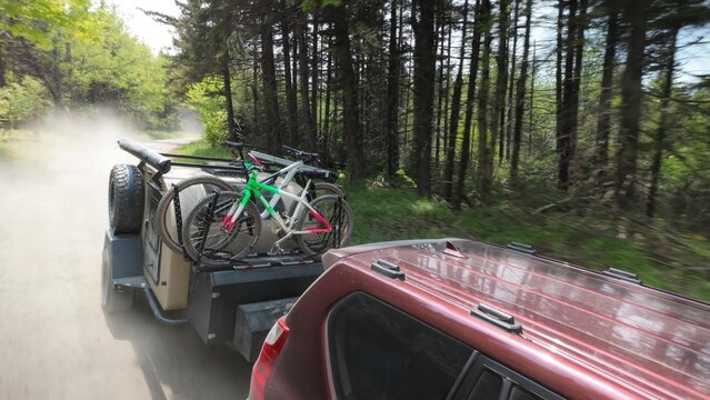 A family drives along a dusty trail in Monongahela National Forest, towing a teardrop trailer with bicycles attached, surrounded by lush trees and serene mountains.