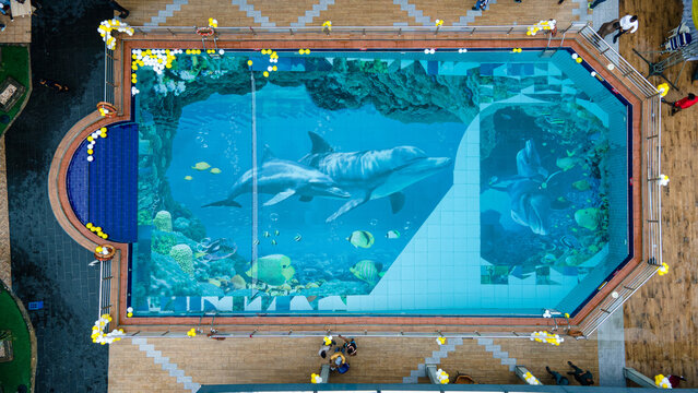 Aerial view of a pristine swimming pool with an underwater-themed mural, sparkling under the sunlight with a realistic dolphin depiction, Port harcourt, Nigeria.
