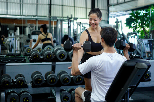 female trainer training male working out with dumbbells weight lifting in gym