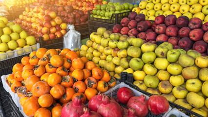 Fresh colorful fruits including apples, persimmons and pomegranates displayed at outdoor market stall, representing healthy nutrition, organic farming, vegan food and natural lifestyle concepts