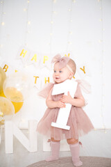 a little blue-eyed girl holds a number one, celebrating her first birthday