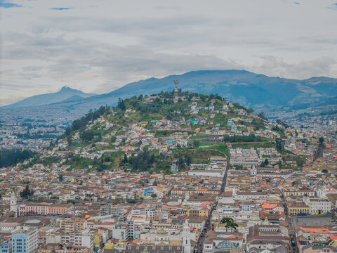 Aerial view of a city nestled between rolling hills and mountains, with El Panecillo towering over the cityscape, Quito, Ecuador.