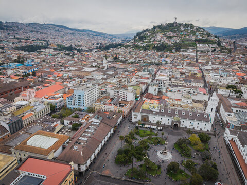 Aerial view of a sprawling cityscape with historic buildings, Metropolitan Cathedral, and vibrant plazas nestled beneath the watchful gaze of Panecillo Hill, Quito, Ecuador.