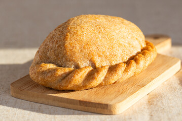 Freshly baked cabbage pie on a wooden board on a table. Russian baked puff pastry with cabbage fillings, sunlight from a window.