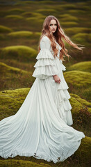 A woman with long red hair wearing a flowing white dress looks back over her shoulder in a green, moss-covered landscape.