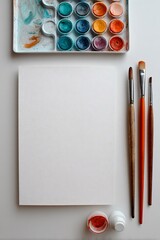 Foglio di carta bianco con tavolozza di acquerelli e tre pennelli di diverse dimensioni, per esaltare la creatività