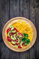 Italian piada - piadina with tomatoes, avocado, bean sprouts, scrambled eggs and cheddar cheese on wooden table. Top view
