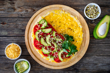 Italian piada - piadina with tomatoes, avocado, bean sprouts, scrambled eggs and cheddar cheese on wooden table. Top view