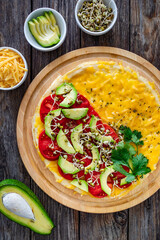 Italian piada - piadina with tomatoes, avocado, bean sprouts, scrambled eggs and cheddar cheese on wooden table. Top view