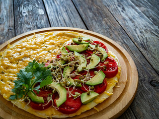 Italian piada - piadina with tomatoes, avocado, bean sprouts, scrambled eggs and cheddar cheese on wooden table	
