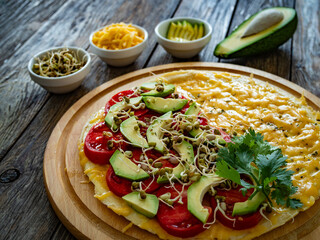 Italian piada - piadina with tomatoes, avocado, bean sprouts, scrambled eggs and cheddar cheese on wooden table	