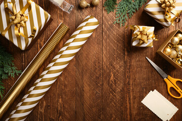 Flat lay of gold and white striped wrapping paper, ribbon, scissors, and small gift boxes on wooden table. Christmas gift wrapping. Copy space.