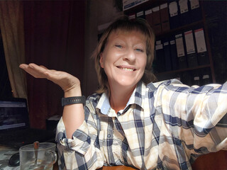 Mature blonde woman taking a cheerful selfie in her cozy workspace during the afternoon