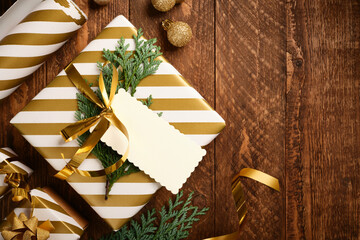 Christmas golden and white gift box with empty rectangular tag on wooden background. Copy space