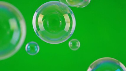 Numerous iridescent soap bubbles float and drift gracefully against a vibrant solid green screen background creating a playful and ethereal visual effect perfect for overlays and creative projects.