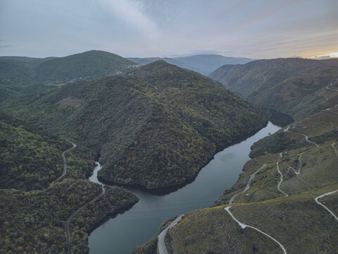 Aerial view of the Sil River winding through the verdant, rugged landscape of Ribeira Sacra, a tapestry of deep greens and reflective blues, Sober, Lugo, Spain.