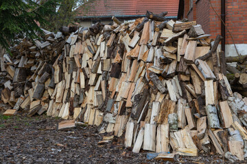 A large stack of freshly chopped firewood piled outdoors near a building, showcasing natural wood texture and variety of logs.
