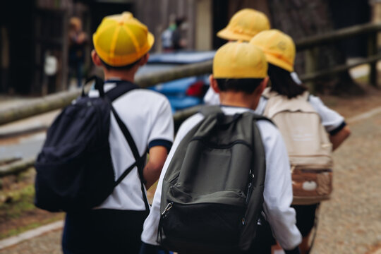 Group of school children students outdoor excursion, guided tour in the city with guide, docent with tourist pupils visitors, wear color caps hats, kids class field trip, urban sightseeing in Japan