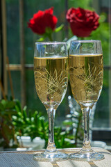 Two champagne glasses with red roses against a backdrop of green foliage for a romantic celebration or Valentine's Day.