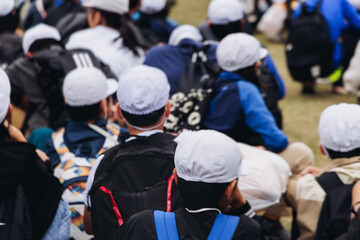 Fototapeta premium Group of school children students outdoor excursion, guided tour in the city with guide, docent with tourist pupils visitors, wear color caps hats, kids class field trip, urban sightseeing in Japan