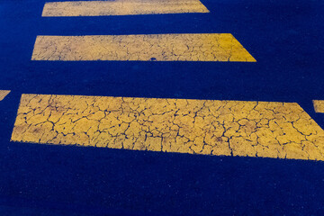 Cracked yellow lines of a pedestrian crossing under evening light create a unique urban scene