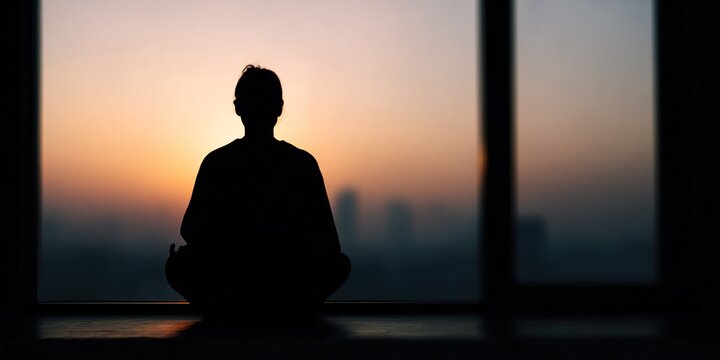 Silhouette of a person meditating during sunset in a serene urban setting