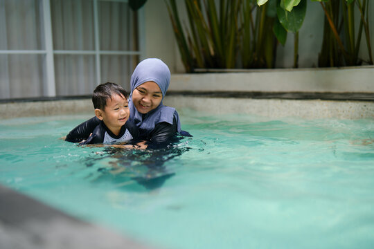 A mother gently supports her little boy as they swim together in the home pool, capturing a joyful family moment.