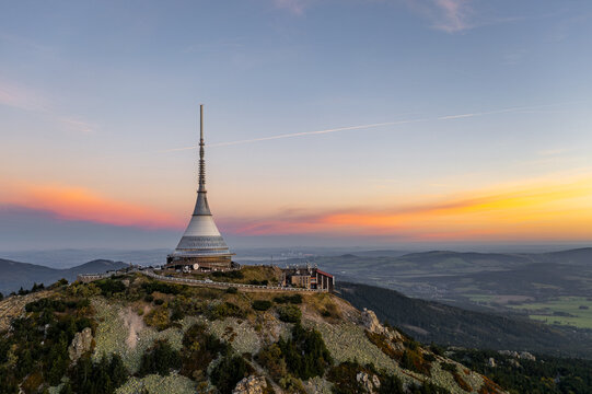 Aerial view of the iconic Jestěd tower piercing the skyline as the sun paints the horizon with fiery hues, Liberec, Liberecky kraj, Czechia.