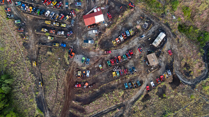 Aerial view of a vehicle graveyard with a mix of colorful cars and trucks scattered amongst the dark earth near Mount Batur, Bali, Indonesia.