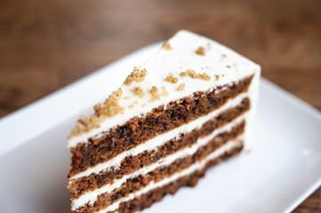 Slice of carrot cake with alternating layers of cake and cream on a plate, highlighting geometric structure and color contrasts.