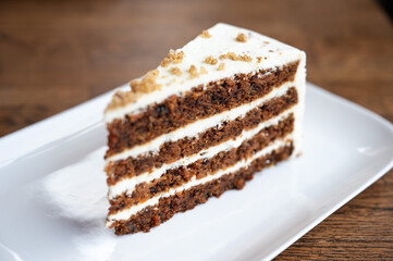 Slice of carrot cake with alternating layers of cake and cream on a plate, highlighting geometric structure and color contrasts.