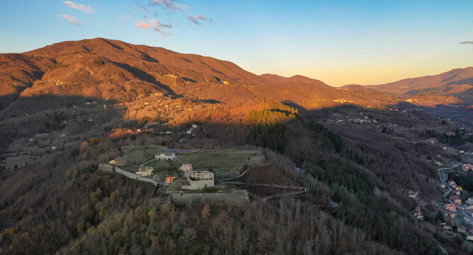 Aerial view of a medieval fortress perched atop a forested hill, bathed in the warm glow of the setting sun, Castelnuovo di Garfagnana, Toscana, Italy.