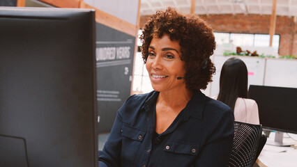 Mature Female Customer Services Agent Working At Desk In Call Center
