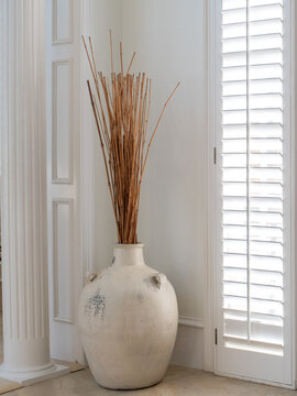 Minimal interior with ceramic urn and bamboo sticks by shuttered window

Category
