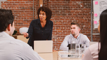 Mature Businesswoman Standing And Leading Office Meeting Around Table
