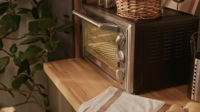 Cropped shot of teenage girl in apron putting baking tray with biscuits in countertop oven learning from mother pasties recipe in cozy kitchen while spending quality time on weekend, slow motion