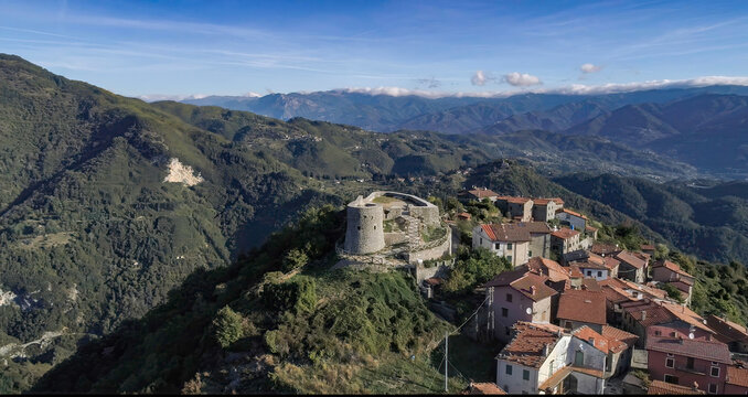 Aerial view of the ancient fortress perched atop a hill amidst terracotta rooftops, embraced by rolling green hills and distant mountains, Trassilico, Tuscany, Italy.