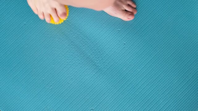 Female feet are doing foot exercises by rolling a prickly massage yellow ball under the foot on the yoga mat pressing down in different sides. Training to correct and relax the foot fascia. 4k footage