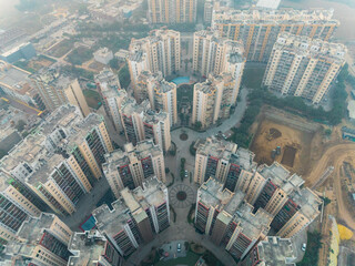 Aerial view of geometric patterns of residential buildings against the hazy sky, casting soft shadows, Gurugram, Haryana, India.