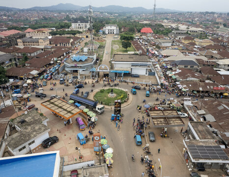 Aerial view of cars and people bustling around a central roundabout and streets lined with buildings under a cloudy sky, Ilesa, Osun, Nigeria.