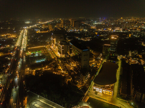 Aerial view of the city illuminated by vibrant lights, contrasting against the dark sky, with identifiable buildings and roads, Gurugram, Haryana, India.