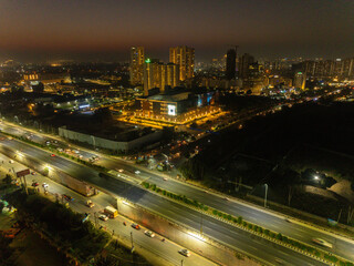 Aerial view of the illuminated Cyber Hub amidst the skyline's glow, with roads and buildings reflecting a vibrant urban pulse, Gurugram, Haryana, India.